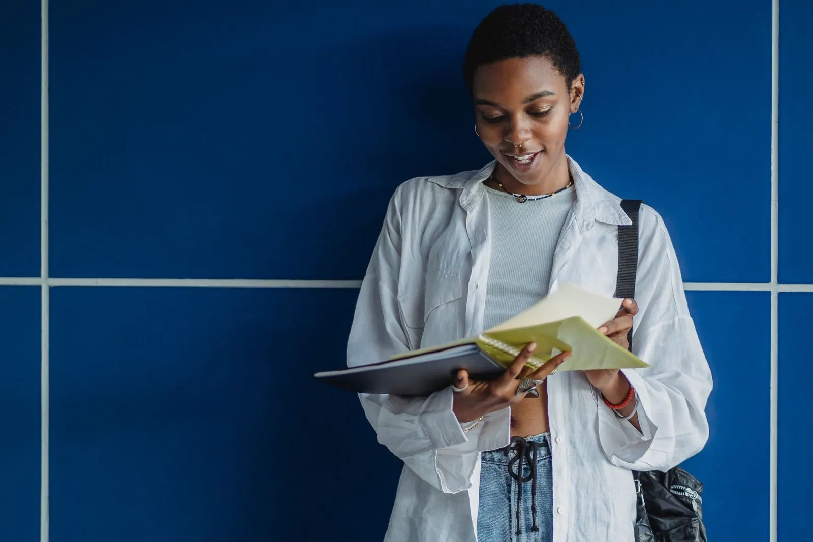 Jeune étudiante qui consulte un carnet, adossée à un mur bleu